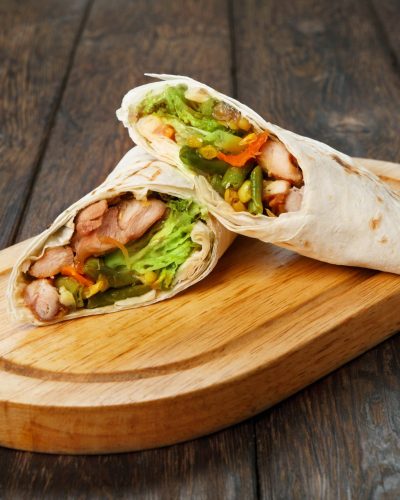 Mexican restaurant fast food - wrapped burritos with chicken and vegetables closeup at wooden desk on table